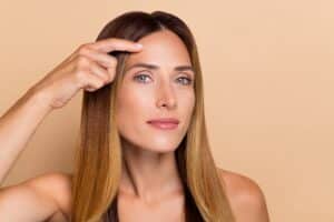 A woman pointing to her forehead after a forehead lift procedure in Hauppauge, NY