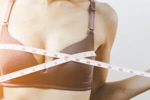 A woman wrapping a tape measure around her chest before breast augmentation