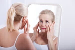 A woman looking in the mirror and considering a MACS facelift in Long Island